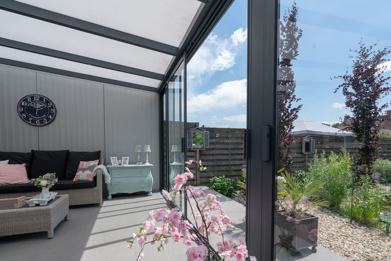 Terrassenüberdachung aus Aluminium, seitlich mit Glasschiebewänden geschlossen, darunter eine Sitzecke