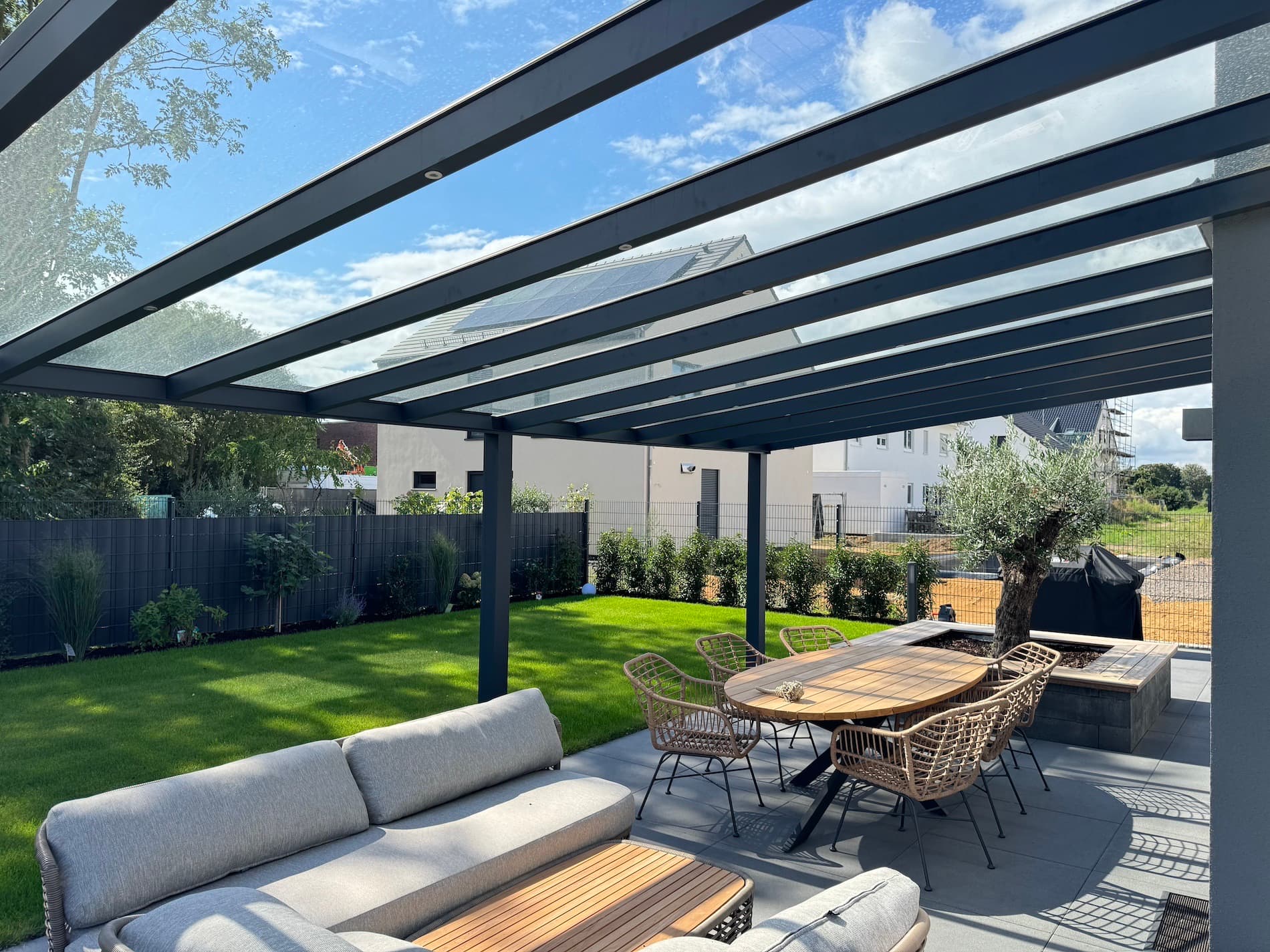 Terrassenüberdachung aus anthrazitfarbenem Aluminium mit Glasdach über einer Terrasse mit Sitzgruppe und Esstisch